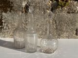 trois bouteilles en verre posées sur une table près d'un mur en pierre