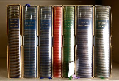 Plusieurs livres sont empilés sur une étagère devant une fenêtre
