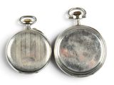 two silver pocket watches sitting side by side on a white surface