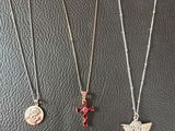 three necklaces with charms on them sitting on a black surface