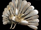 a silver peacock brooch made of spoons on a black background