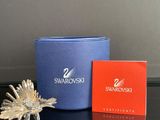 une petite fleur en argent posée sur une table, à côté d'une boîte de Swarovski