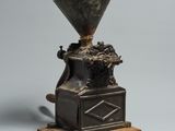 un moulin à café ancien posé sur un socle en bois, sur fond gris