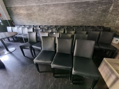 des rangées de chaises noires dans une pièce, avec un mur de briques en arrière-plan