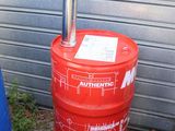 un fût rouge muni d'une pompe, placé à côté d'une poubelle bleue