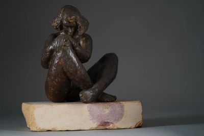 statue of a woman sitting on a rock with her hands on her face