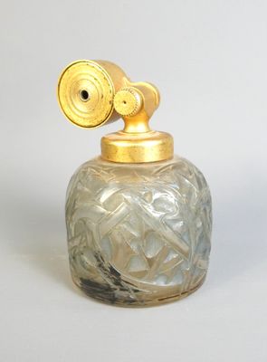 un petit bocal en verre avec un couvercle doré posé sur une surface blanche