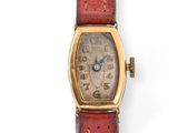 an image of a wrist watch with a gold case and red leather strap
