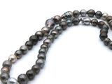 a close up of a strand of black pearls on a white surface