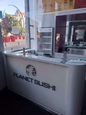 un comptoir blanc sur lequel est accrochée une enseigne indiquant « Planet Sushi »