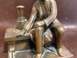 bronze statue of a man sitting on a bench with a vase