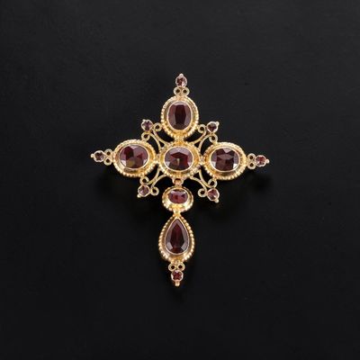 a gold and garnet stone cross pendant on a black background