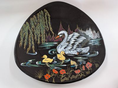 a black plate with a painting of a swan and ducklings on it