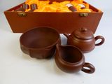 three cups and a teapot sitting next to a box of oranges