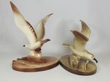 two figurines of seagulls sitting on top of a wooden base