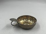 une petite tasse en argent contenant une cuillère, posée sur une surface blanche
