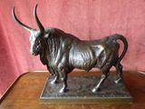 bronze statue of a bull on a wooden table against a red background