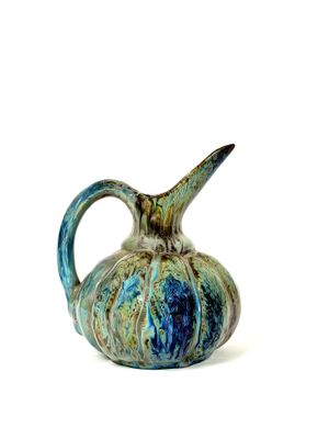 un vase bleu et vert muni d'une anse, posé sur une surface blanche