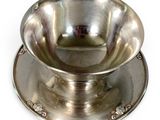 a silver bowl on a saucer on a white surface