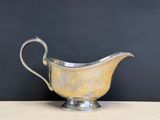an antique silver plated gravy with a curved handle on a wooden table