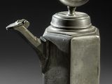 a silver teapot with a circular handle on a gray surface