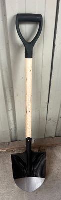 une pelle noire avec un manche en bois accrochée au mur