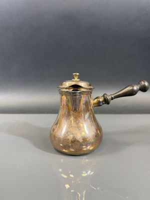 une cafetière ancienne en laiton avec une poignée en bois, posée sur une table