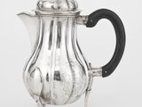 une théière ancienne en argent avec une poignée noire sur fond blanc