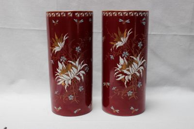 une paire de vases rouges ornés de motifs floraux, posés sur une surface blanche