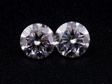 a pair of round cut diamonds on a black surface