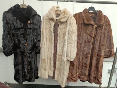 three coats of fur are hanging on a rack in a room