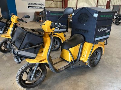Des trottinettes jaunes sont garées dans un entrepôt, avec des cartons à l'arrière