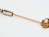 a gold pin with a pearl in it on a white surface