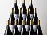 six bouteilles de vin sont posées sur une table devant un mur blanc