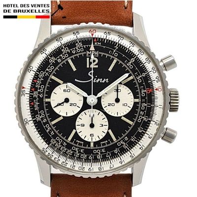 La montre est noire et blanche, avec un bracelet en cuir marron.