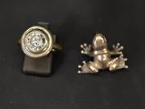 two rings with a frog and a diamond sitting on a black surface