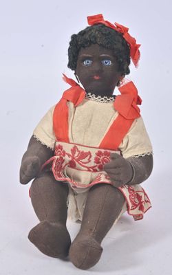 une poupée noire assise sur une surface blanche, vêtue d'une robe rouge et blanche