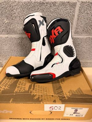 the pair of white and black motorcycle boots are on top of a cardboard box