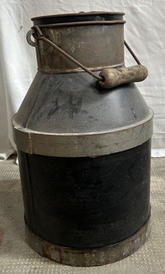 un bidon à lait noir et argent posé par terre