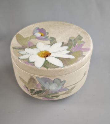 une petite boîte ronde sur laquelle est peinte une fleur