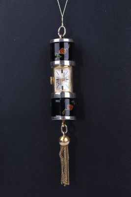une horloge noire et dorée à laquelle est suspendu un pompon au bout de sa chaîne