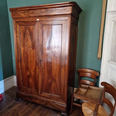 une armoire en bois placée dans un coin de la pièce, à côté d'un fauteuil
