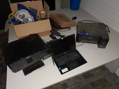 une table sur laquelle se trouvent un ordinateur portable, une imprimante et d'autres appareils électroniques