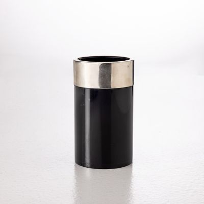 une image représentant un vase noir et argenté posé sur une surface blanche