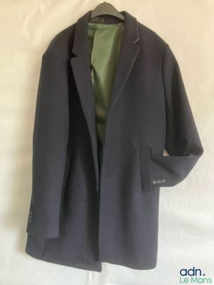 grey coat on a hanger on a white sheet with a green shirt underneath it