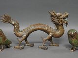 trois figurines en bronze représentant des oiseaux et un dragon sur fond gris
