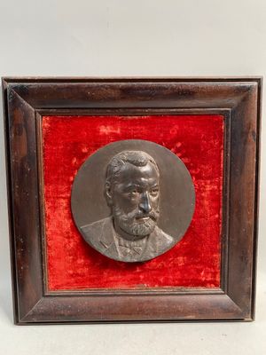 une plaque en bronze représentant un homme barbu, dans un cadre en bois