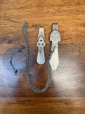 two pieces of silver jewelry sitting on top of a wooden table