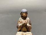 statue of a person sitting on a rock with a hat on