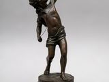 une statue antique en bronze représentant un garçon tenant une raquette de tennis